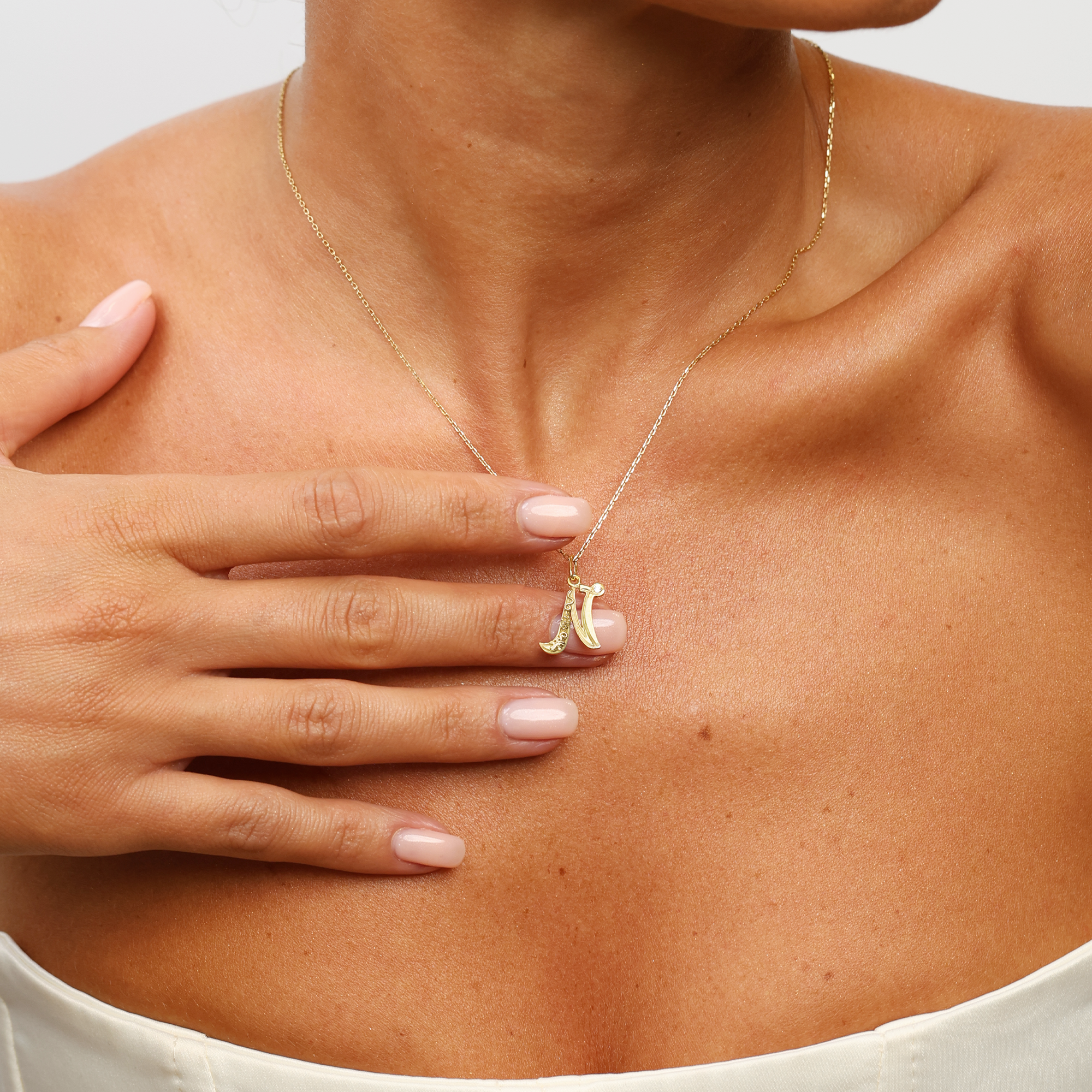 Gold necklace with a pendant worn by a person, with a hand touching the chest.