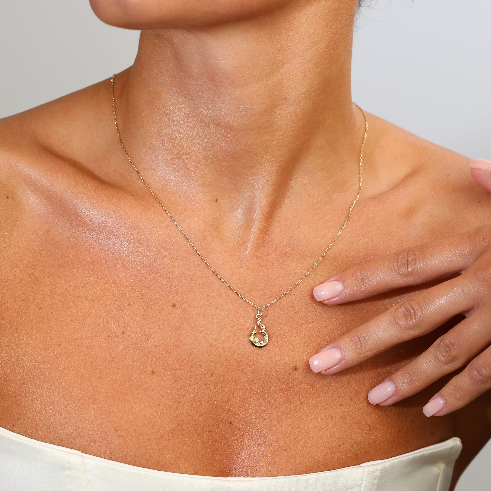 Gold necklace with a pendant worn by a person, with a hand touching the shoulder.