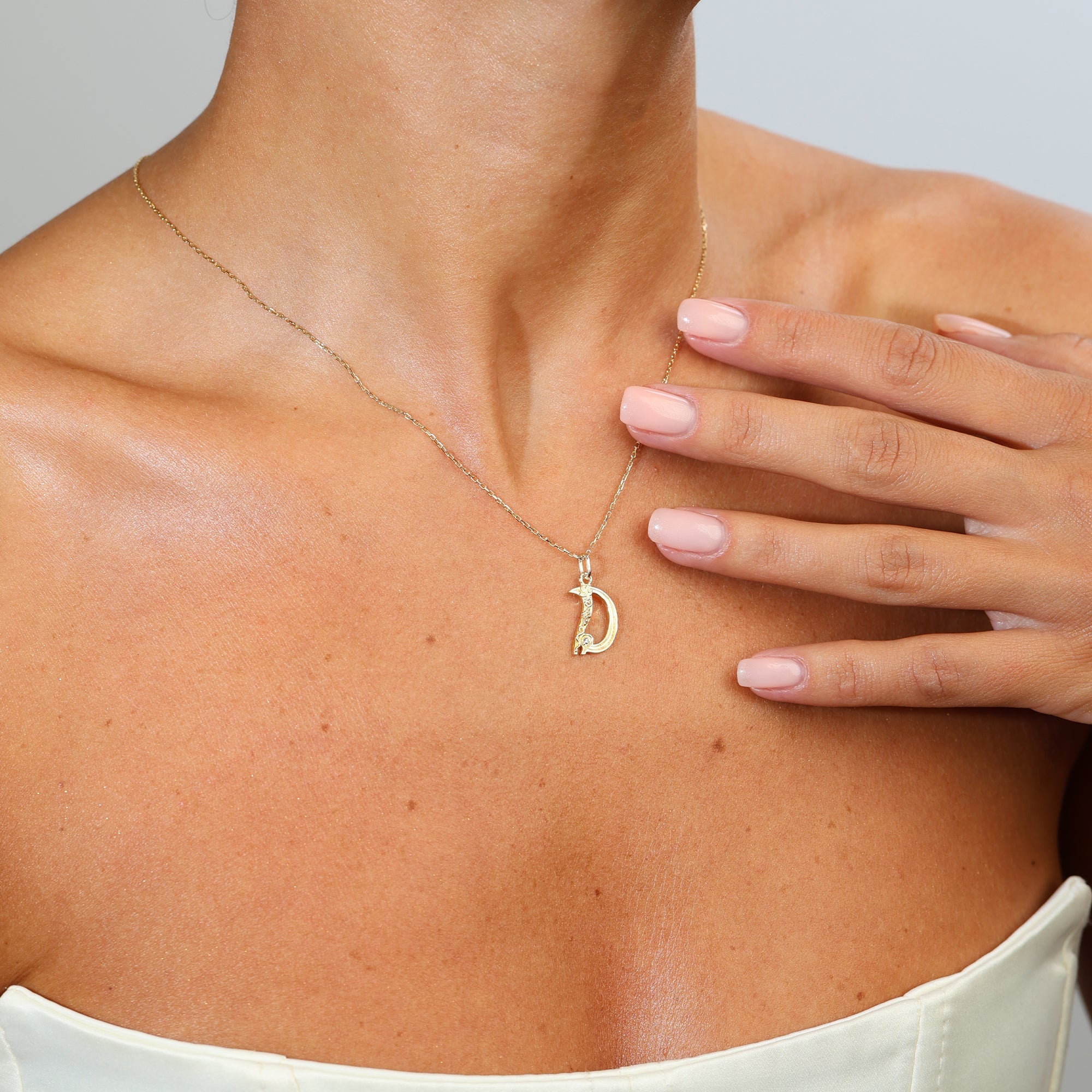 Gold necklace with a 'D' pendant worn by a person, with a hand touching the neck.