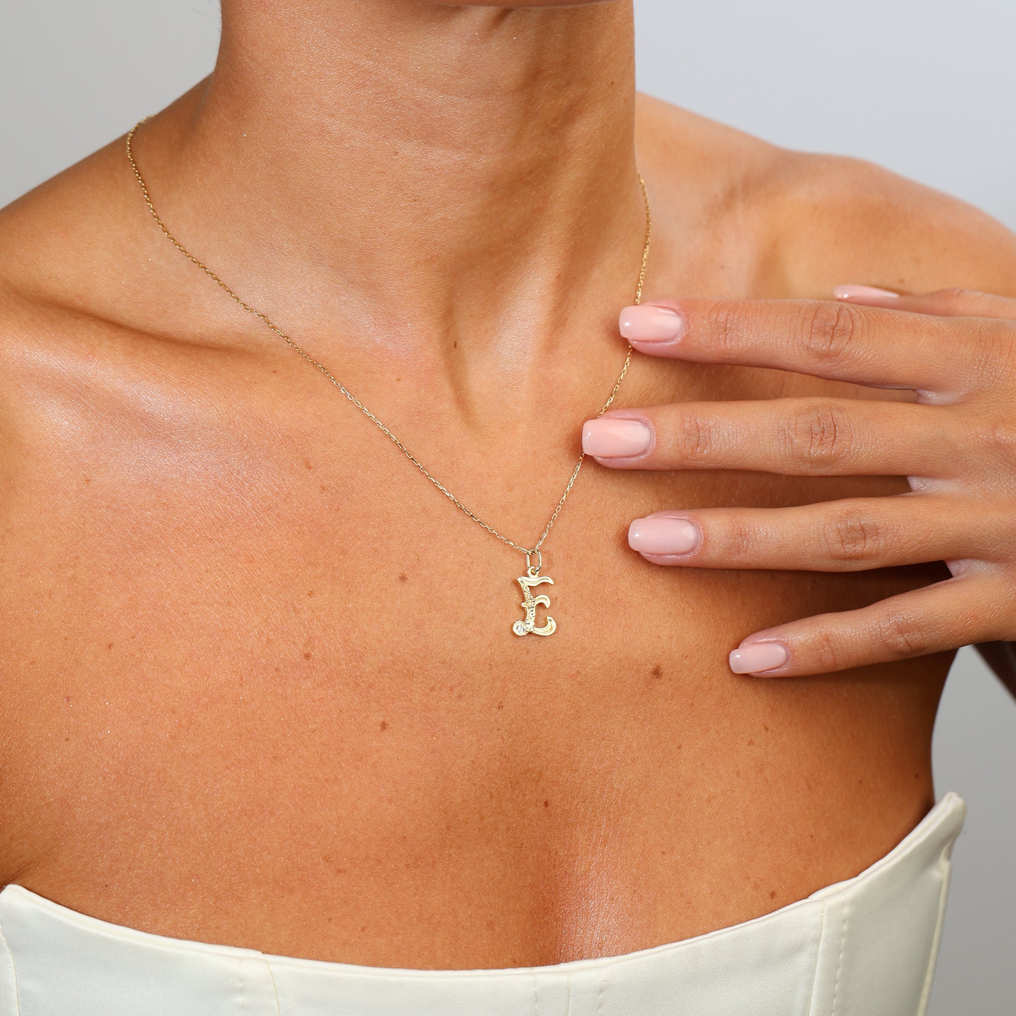 Gold necklace with a letter 'E' pendant worn by a person, with a hand touching the neck.
