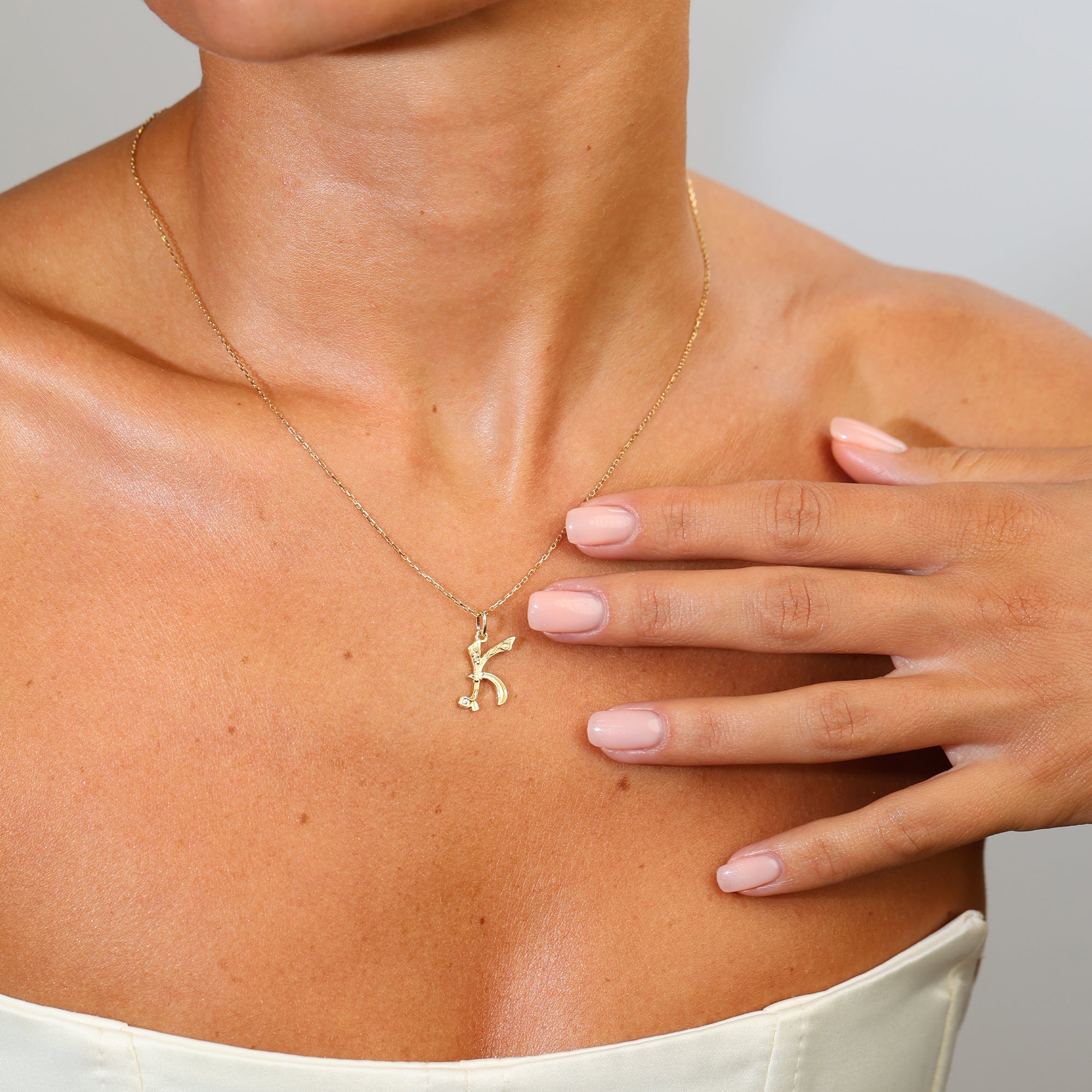 Gold necklace with a pendant worn by a person, with a hand touching the chest.