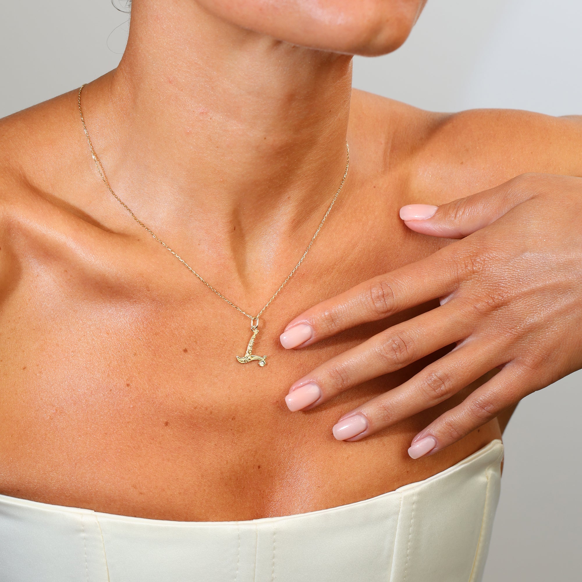 Woman wearing a gold necklace with a small pendant on a neutral background