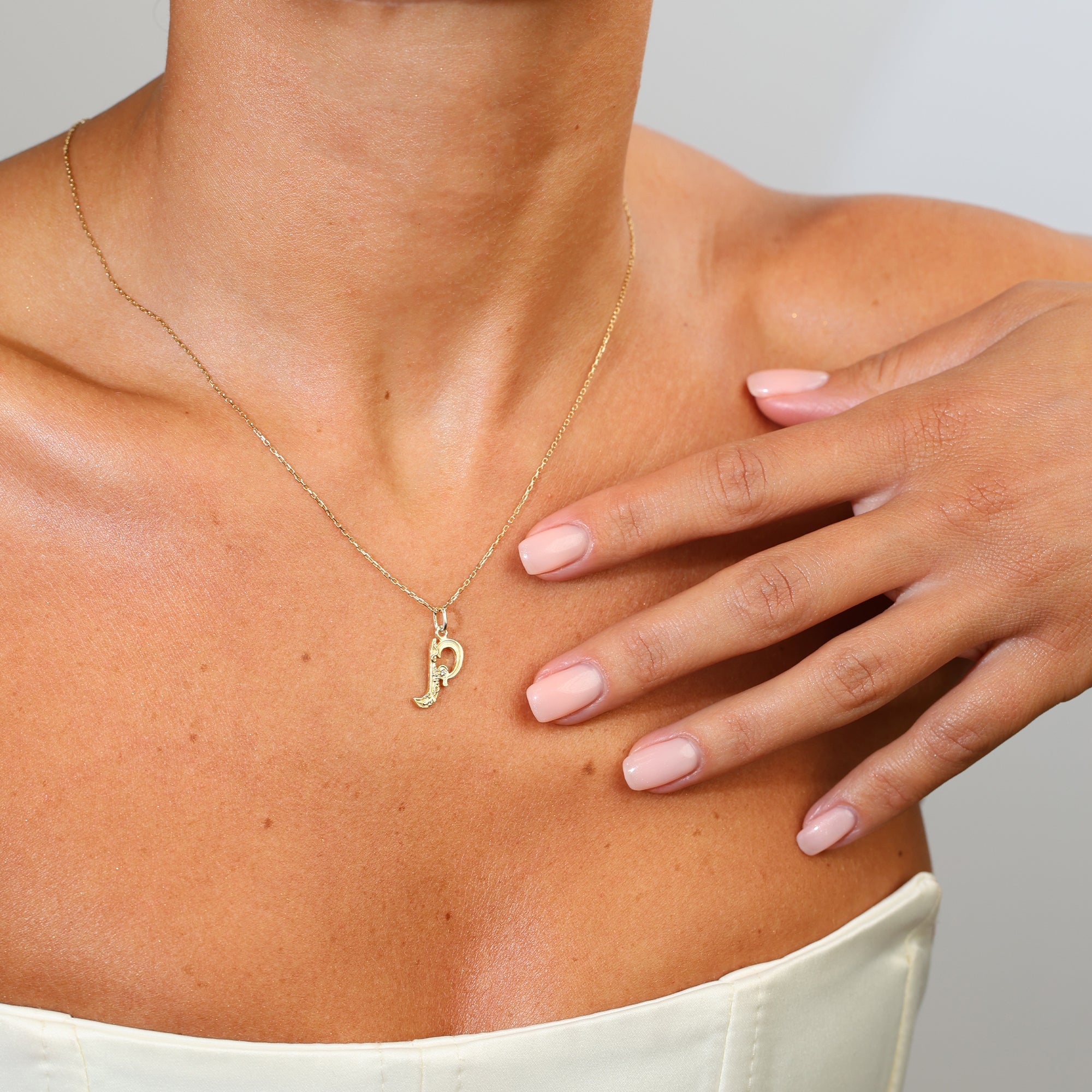 Gold necklace with a letter 'P' pendant on a person's neck with a hand touching their shoulder.