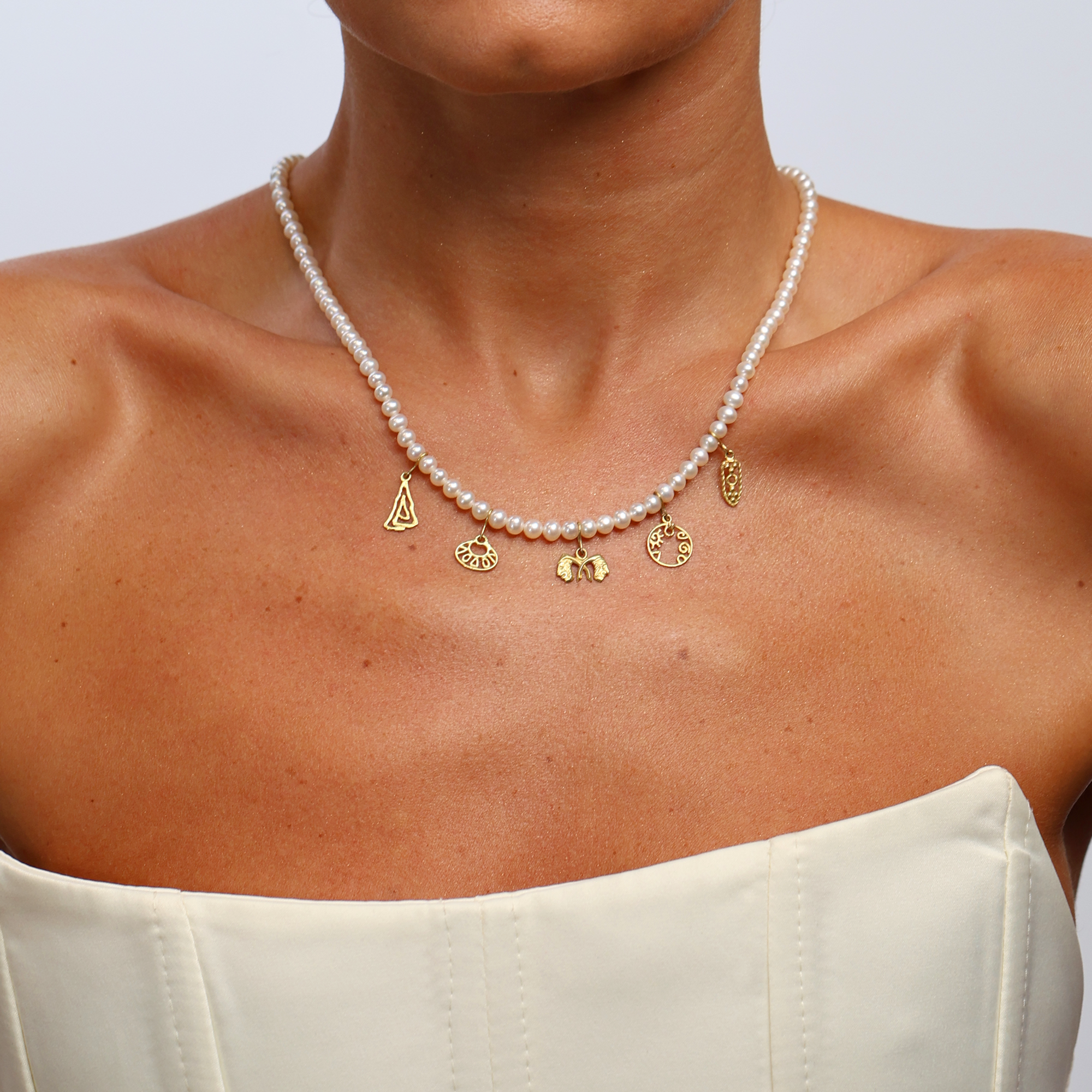 Pearl necklace with gold charms on a person wearing a white top against a light background