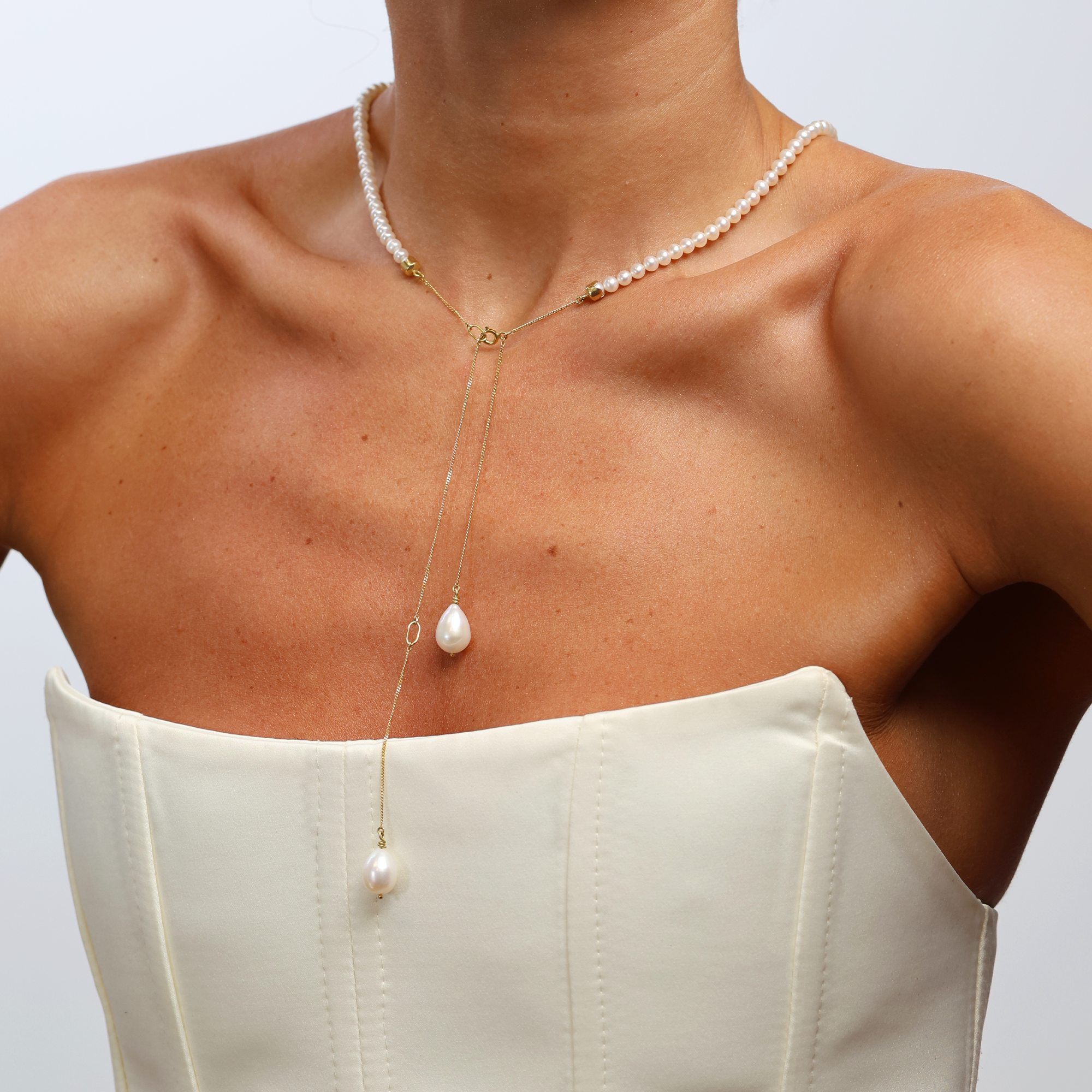 Pearl necklace with a pendant on a person wearing a white top against a light gray background