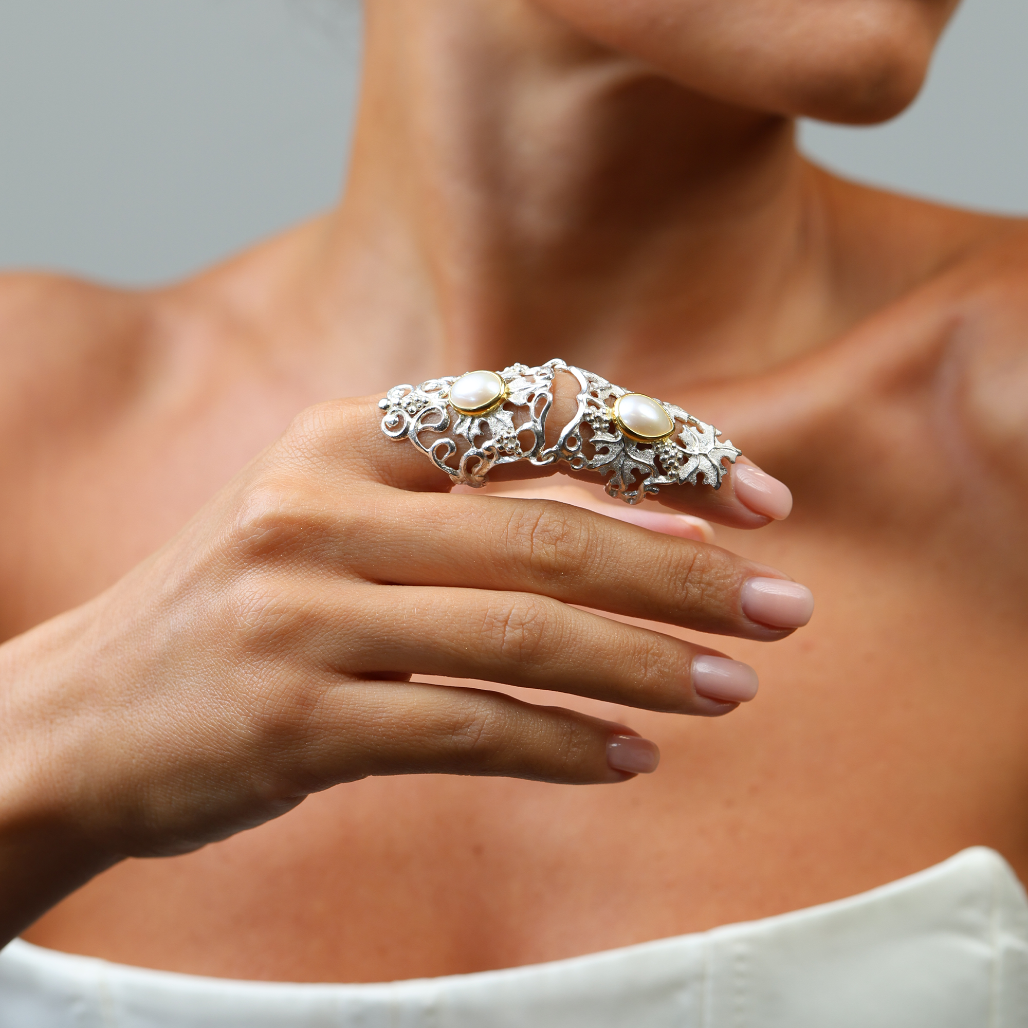 Close-up of a hand wearing a decorative armor ring with pearls against a neutral background