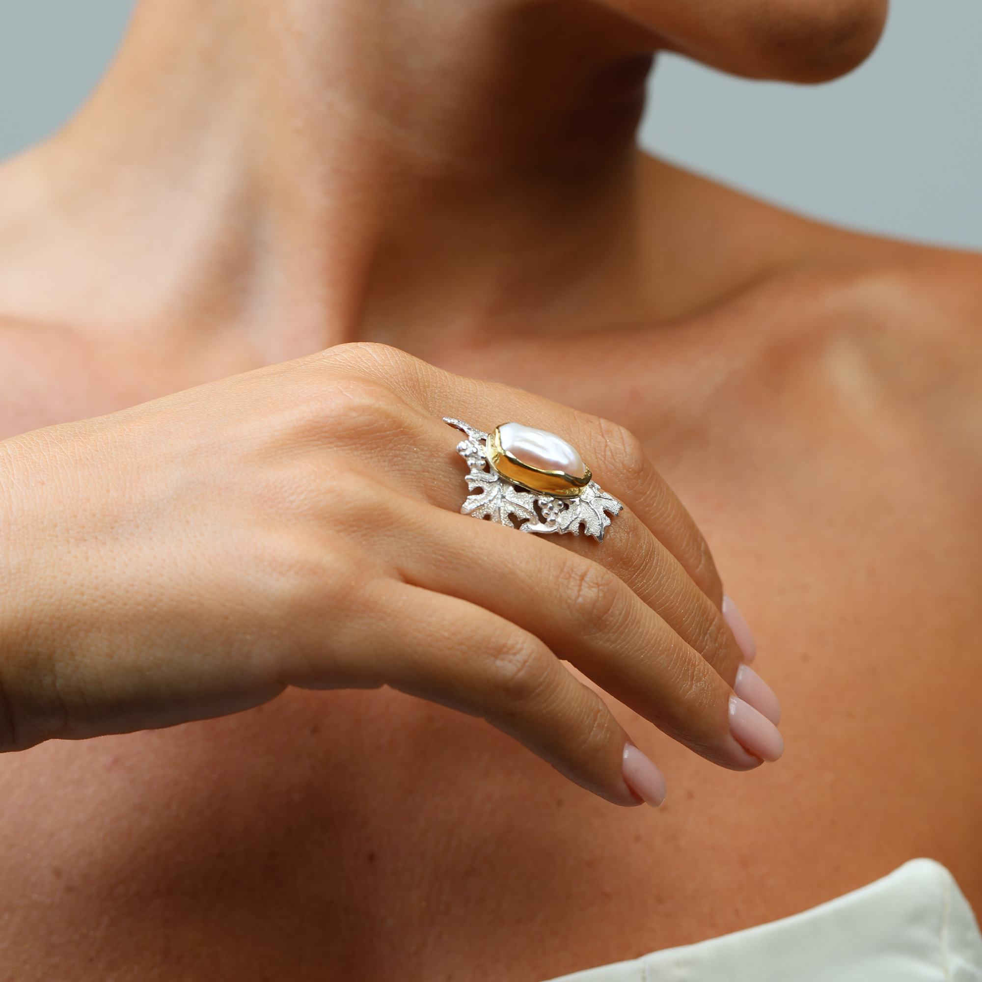 Close-up of a hand wearing a ring with a large pearl on a neutral background