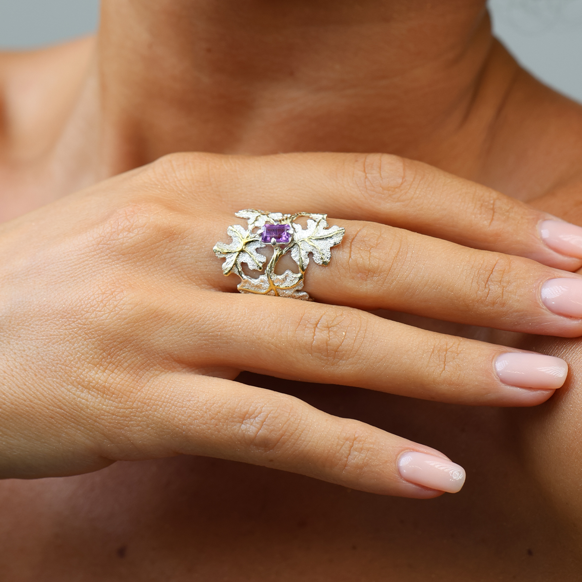Hand wearing a silver ring with a purple gemstone against a neutral background