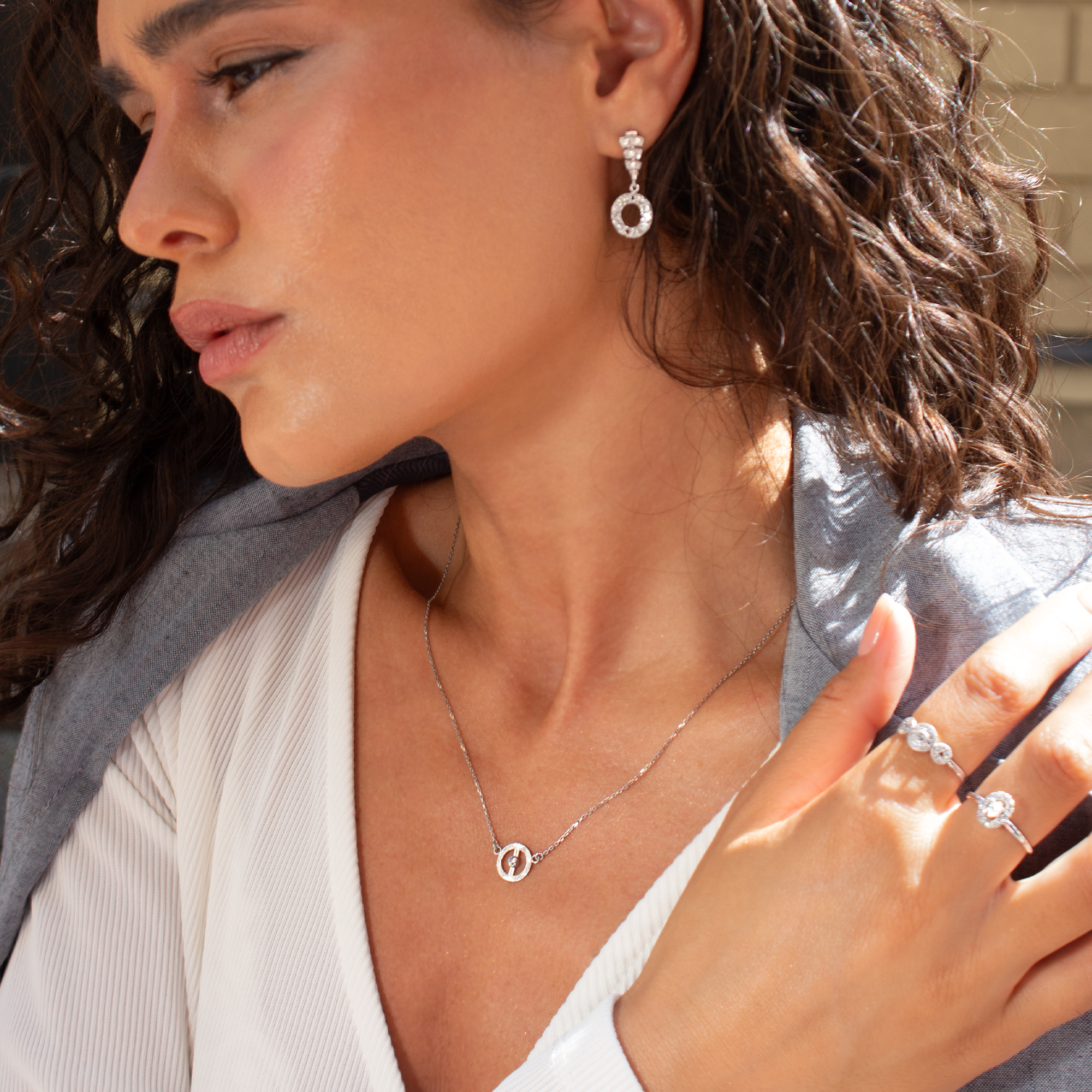 Woman wearing silver jewelry including diamond earrings, necklace, and ring.