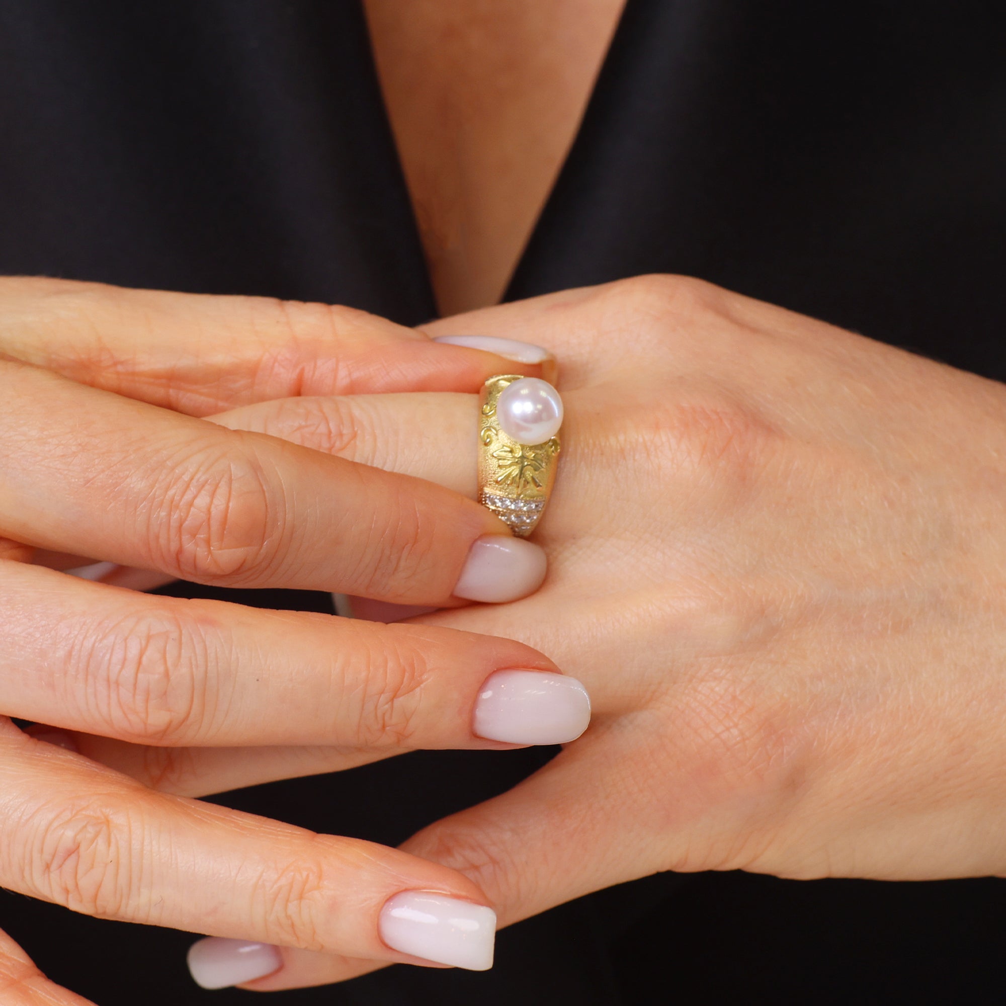 Close-up of a hand wearing a gold ring with a pearl on a black background